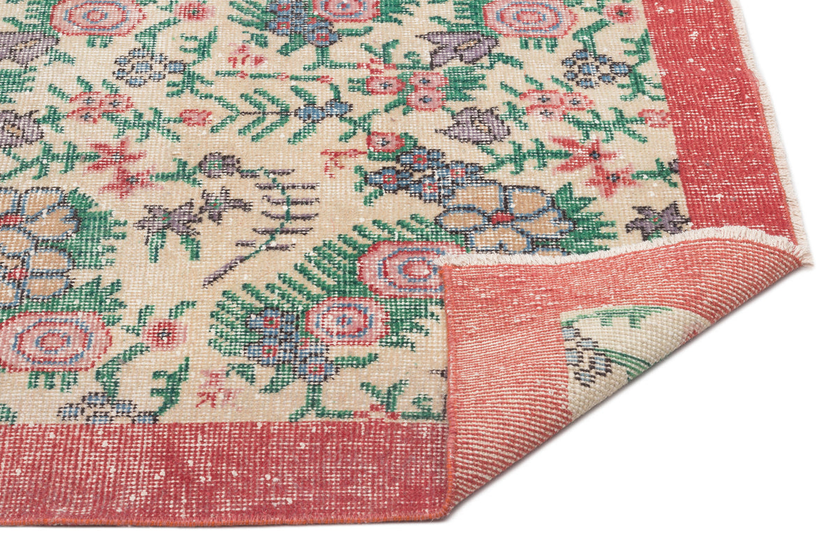 Beige rug with a distressed floral pattern in red, green, and blue, featuring a wide red border and a folded corner.