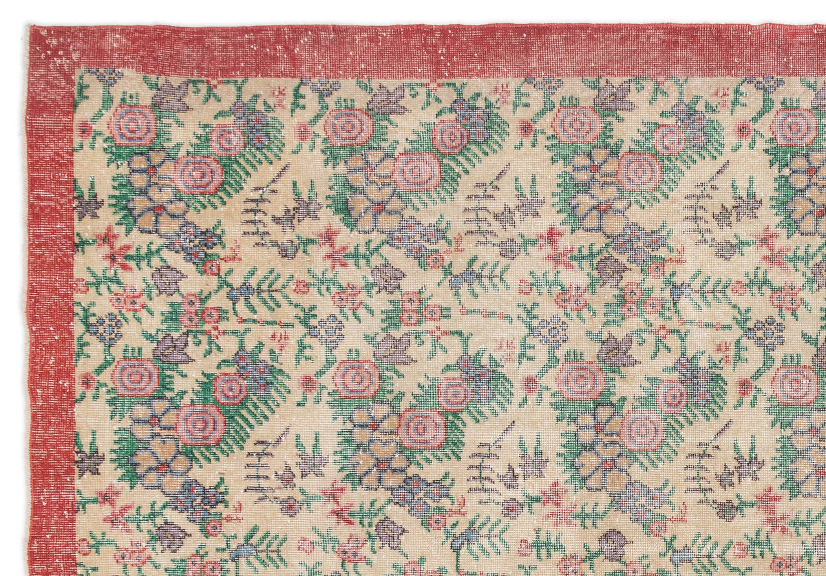 Beige rug with a red border and a repeating floral pattern in pink, green, and blue.