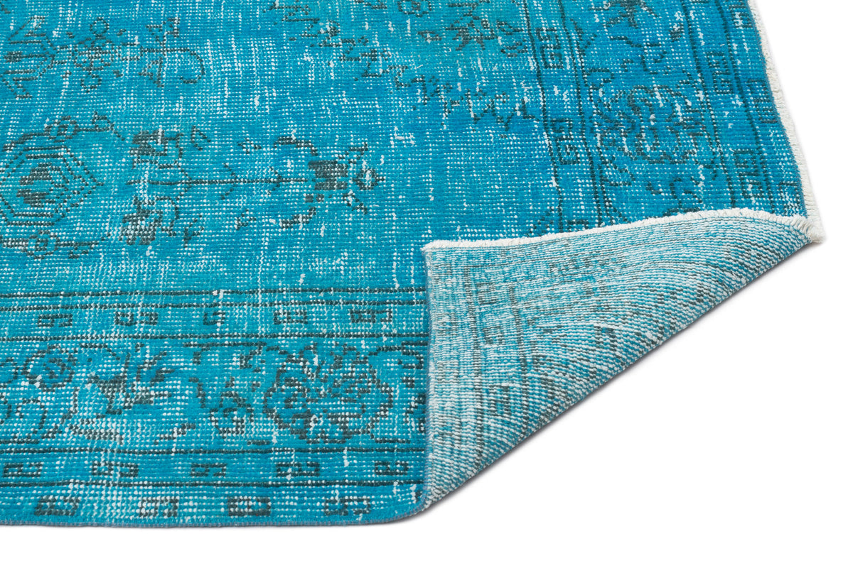 Bright turquoise distressed rug with a faded dark grey traditional medallion pattern, shown with a folded corner.