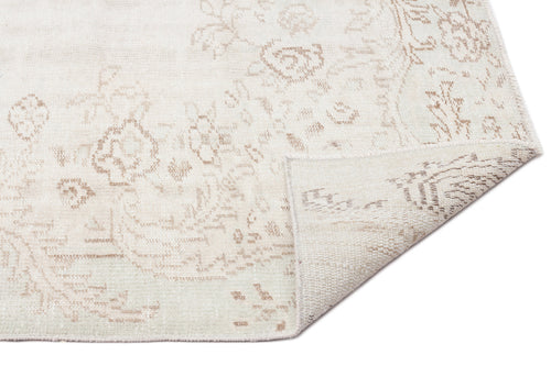 Load image 1 in gallery view. Off-white rug with a faded beige floral medallion pattern and a corner folded over to reveal the woven backing.