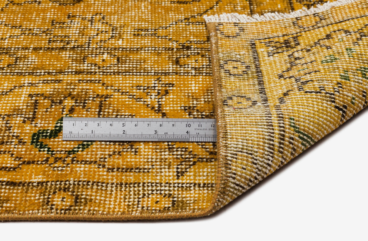 Mustard yellow and brown distressed traditional rug with a folded corner and a metal ruler for scale.