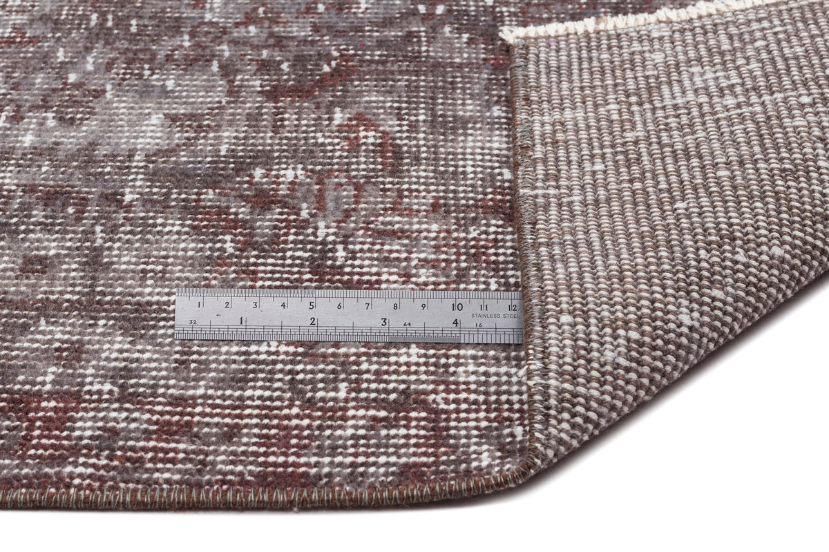 Distressed brown and grey rug with a faded traditional pattern, showing the woven backing and a metal ruler for scale.