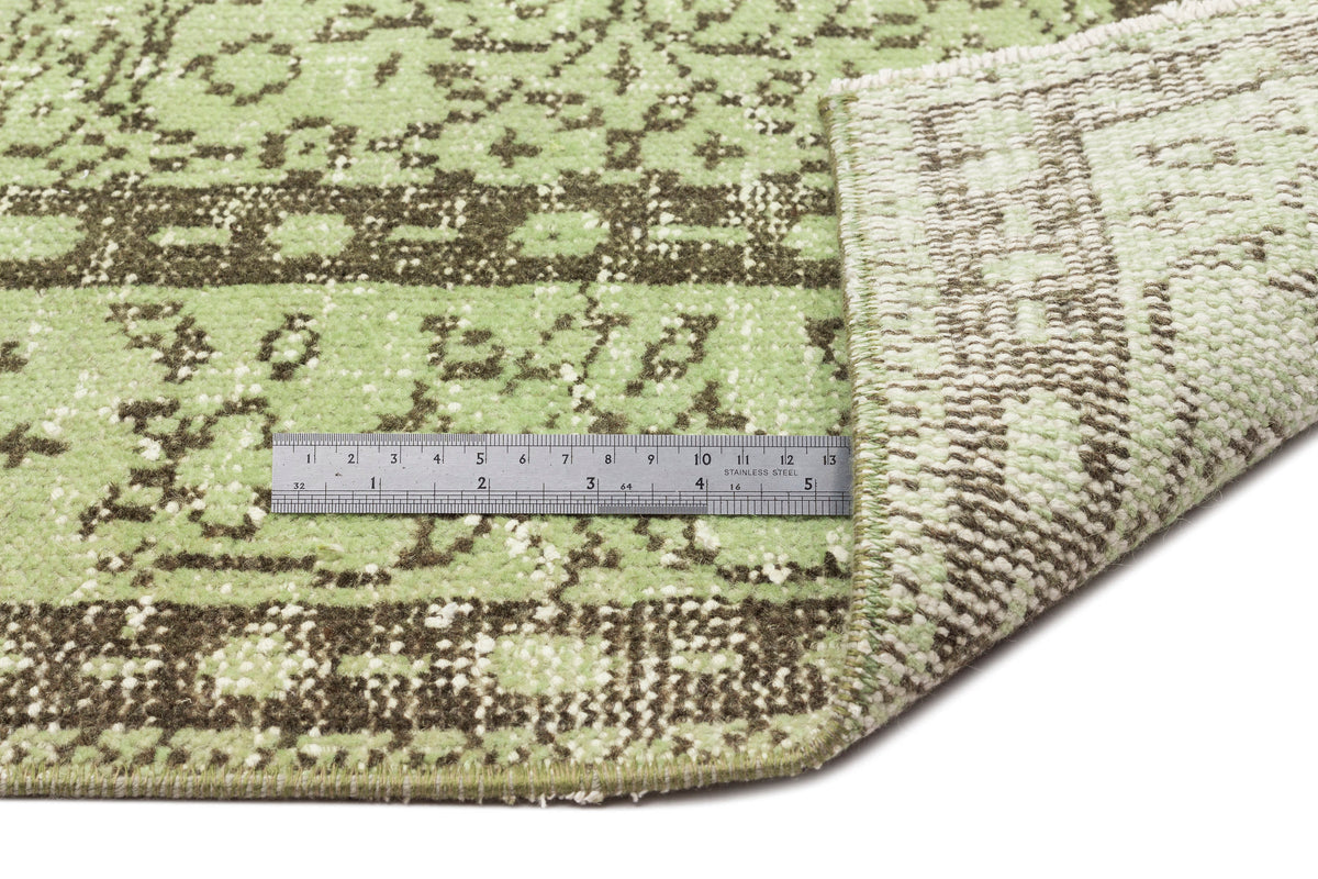 Light green and dark brown distressed traditional rug with a folded corner and a metal ruler for scale.