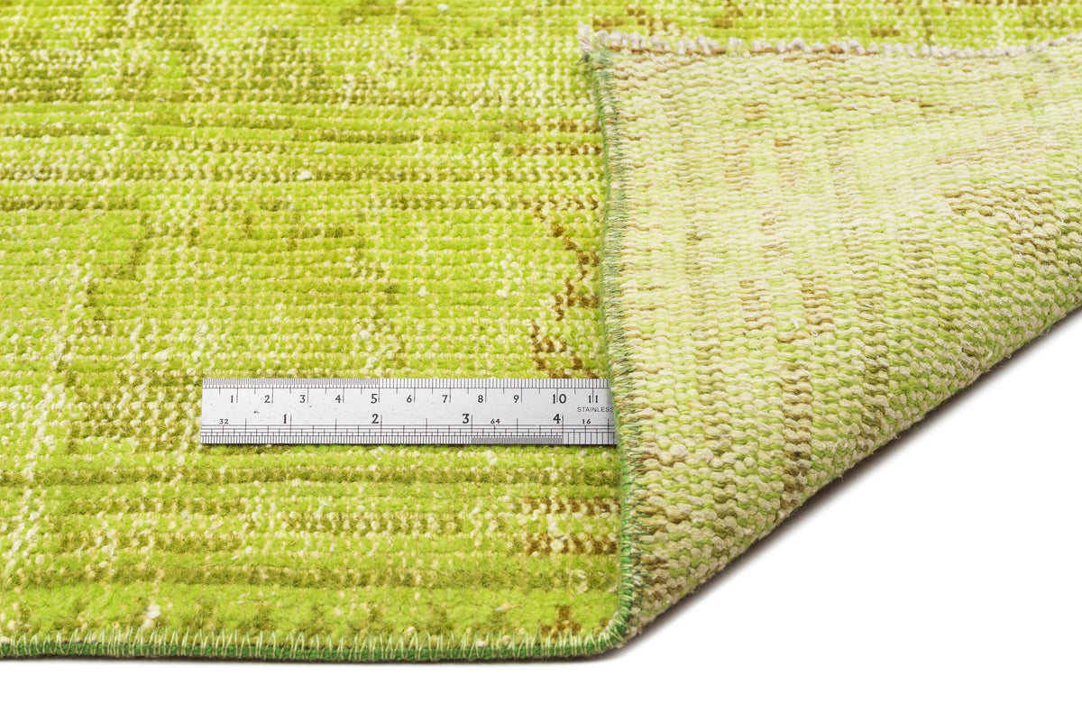 Lime green distressed rug with a faded traditional pattern, shown with a corner folded over and a metal ruler.