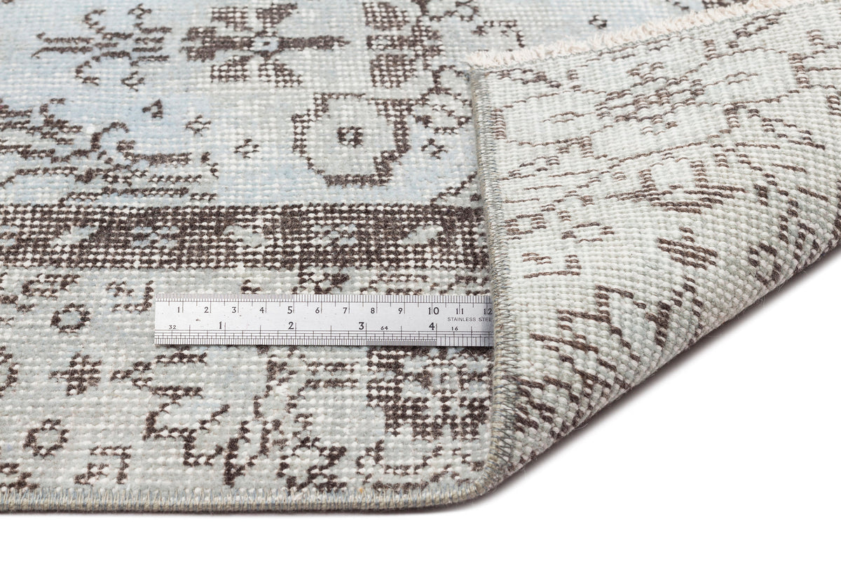 Light blue and brown distressed traditional pattern rug with a folded corner and a metal ruler for scale.