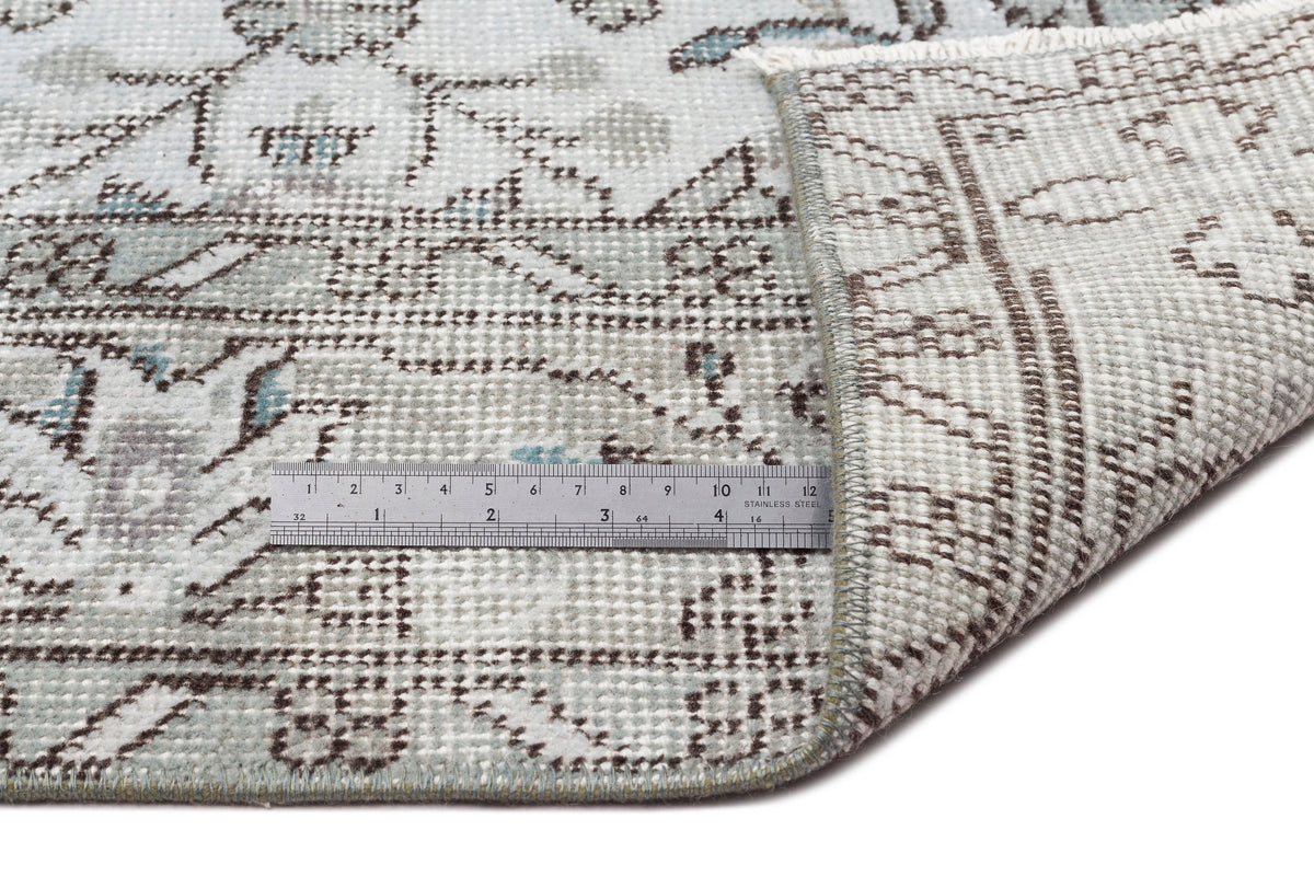 Light blue and brown distressed floral rug with a folded corner and a metal ruler for scale on a white background.