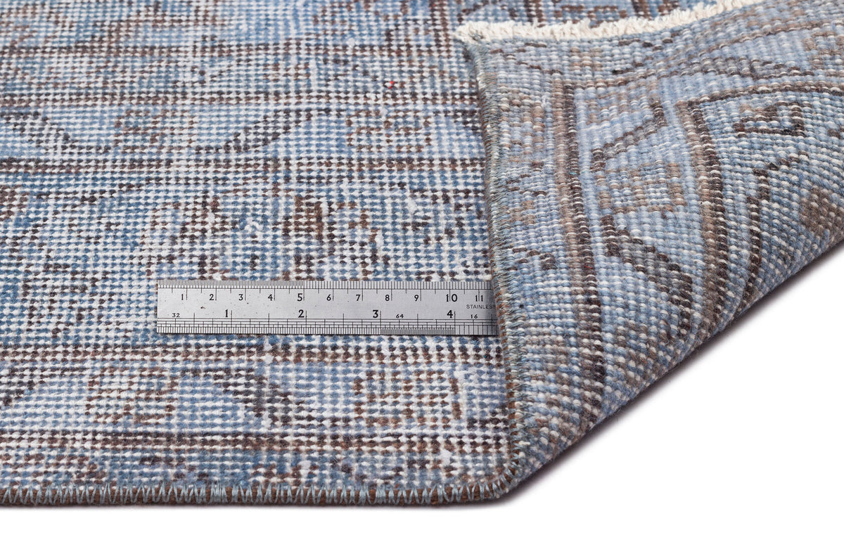 Blue and brown distressed medallion rug with a folded corner showing the weave and a metal ruler for scale.
