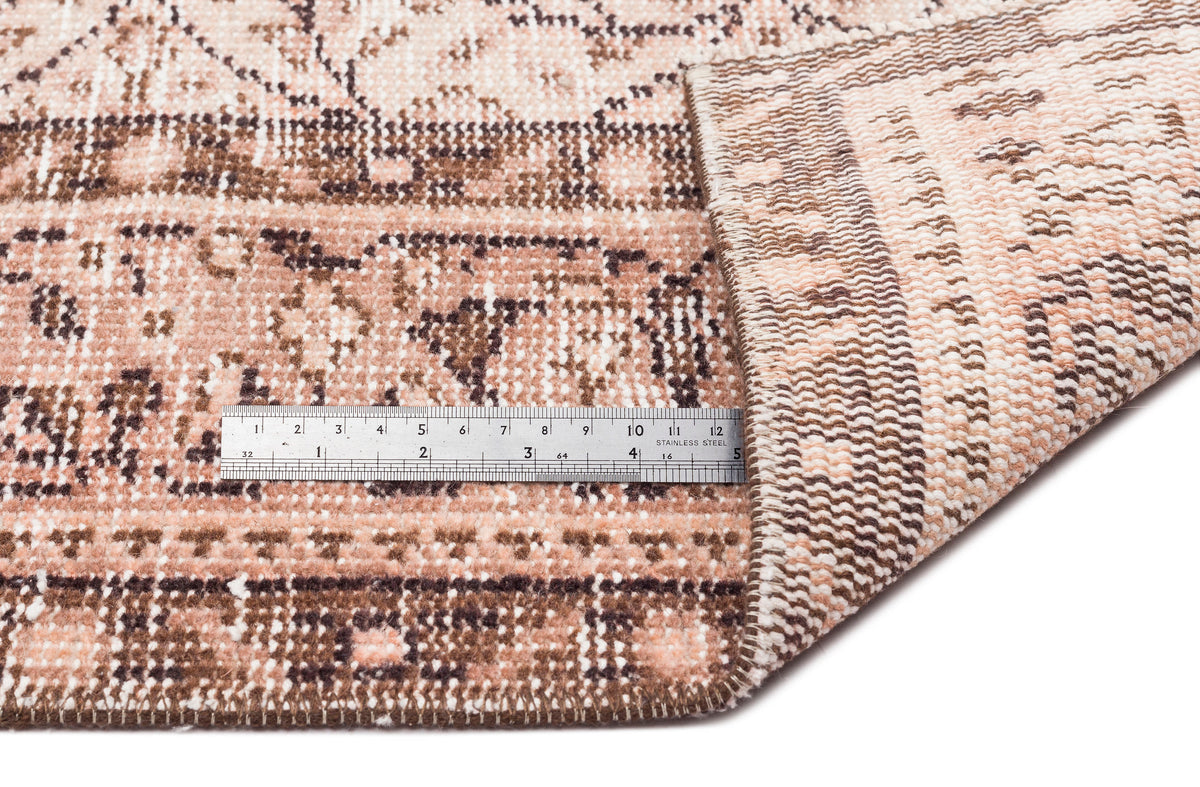 Distressed blush and brown traditional patterned rug with a folded corner and a metal ruler for scale.