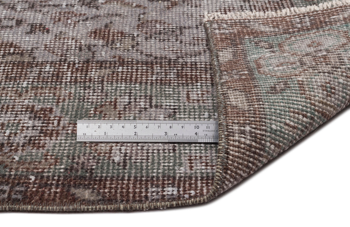 Distressed brown, grey, and sage green vintage-style rug with a folded corner and a metal ruler for scale.