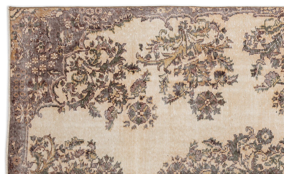 A close-up of the Detiar - Vintage Medallion Rug (5'9 x 9'5) shows its faded floral pattern in muted browns, greens, and beiges, with intricate border details along the top edge.
