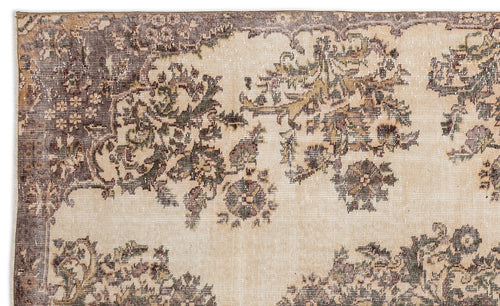Load image 1 in gallery view. A close-up of the Detiar - Vintage Medallion Rug (5'9 x 9'5) shows its faded floral pattern in muted browns, greens, and beiges, with intricate border details along the top edge.