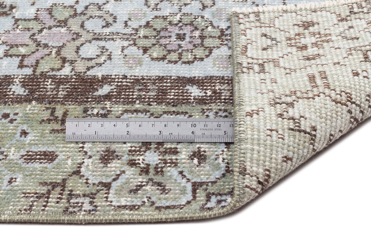 Light blue, sage green, and brown floral medallion rug with a folded corner and a metal ruler for scale.