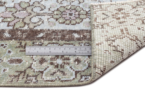 Load image 1 in gallery view. Light blue, sage green, and brown floral medallion rug with a folded corner and a metal ruler for scale.