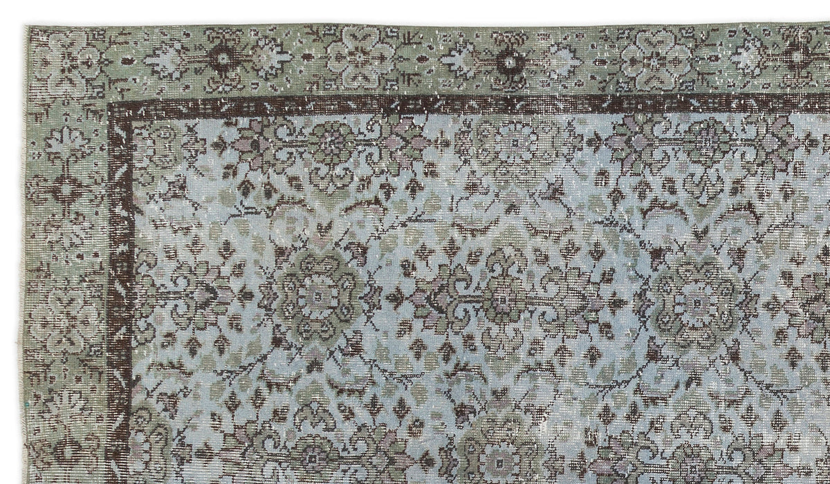 Distressed sage green and light blue rug with a dark brown floral medallion pattern and a decorative border.