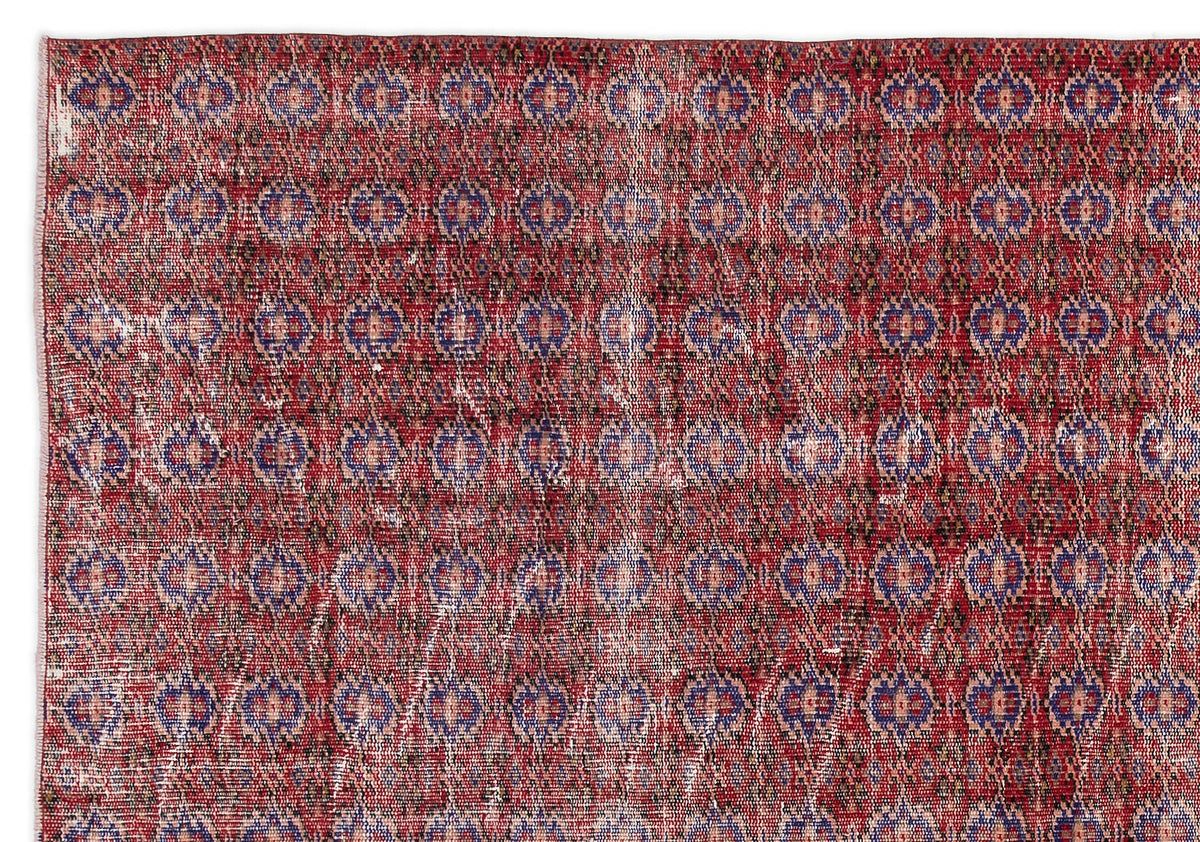 Distressed red rug with a repeating blue and beige geometric medallion pattern.