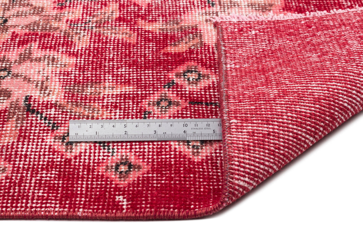 Red and pink distressed floral medallion rug with a folded corner and a stainless steel ruler for scale.