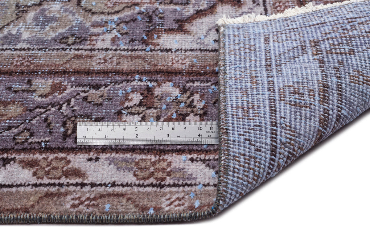 Brown and blue distressed traditional rug with a floral medallion pattern, showing the underside and a metal ruler.