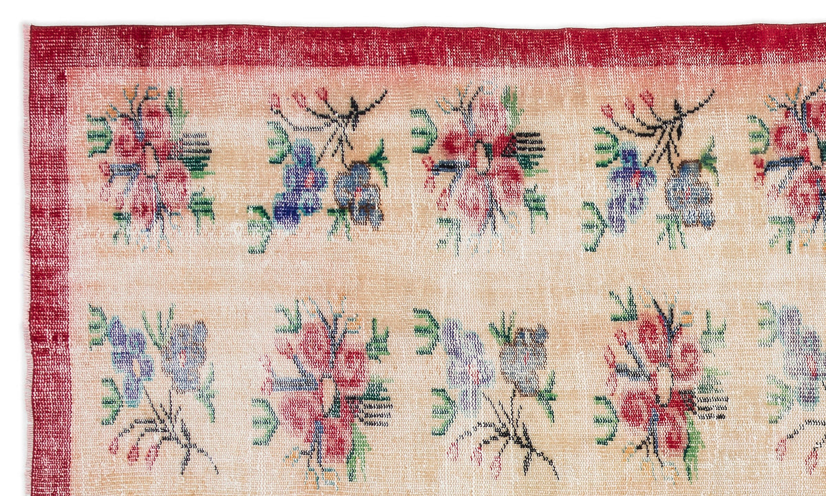 Beige rug with a red border and a repeating pattern of small, multicolored floral motifs.