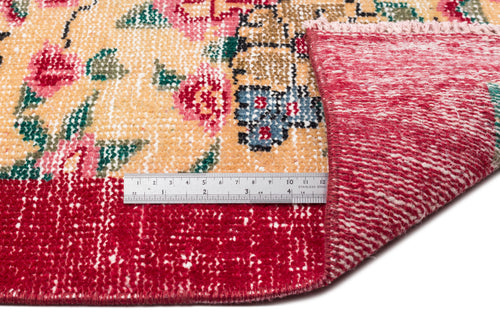 Load image 1 in gallery view. Floral patterned rug with a yellow field and red border, shown folded to reveal the underside with a metal ruler.