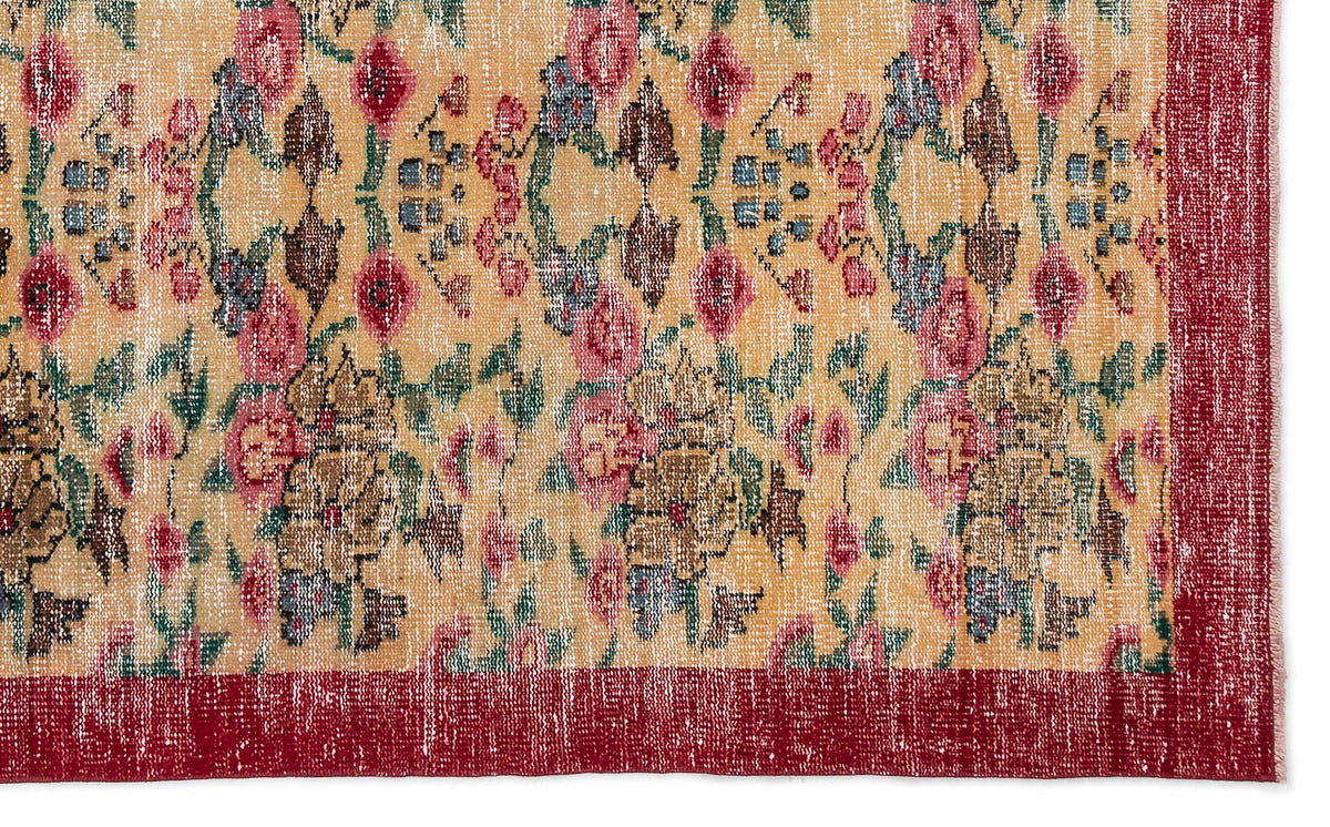 Distressed yellow rug with a floral pattern in red, green, and brown, featuring a solid red border.