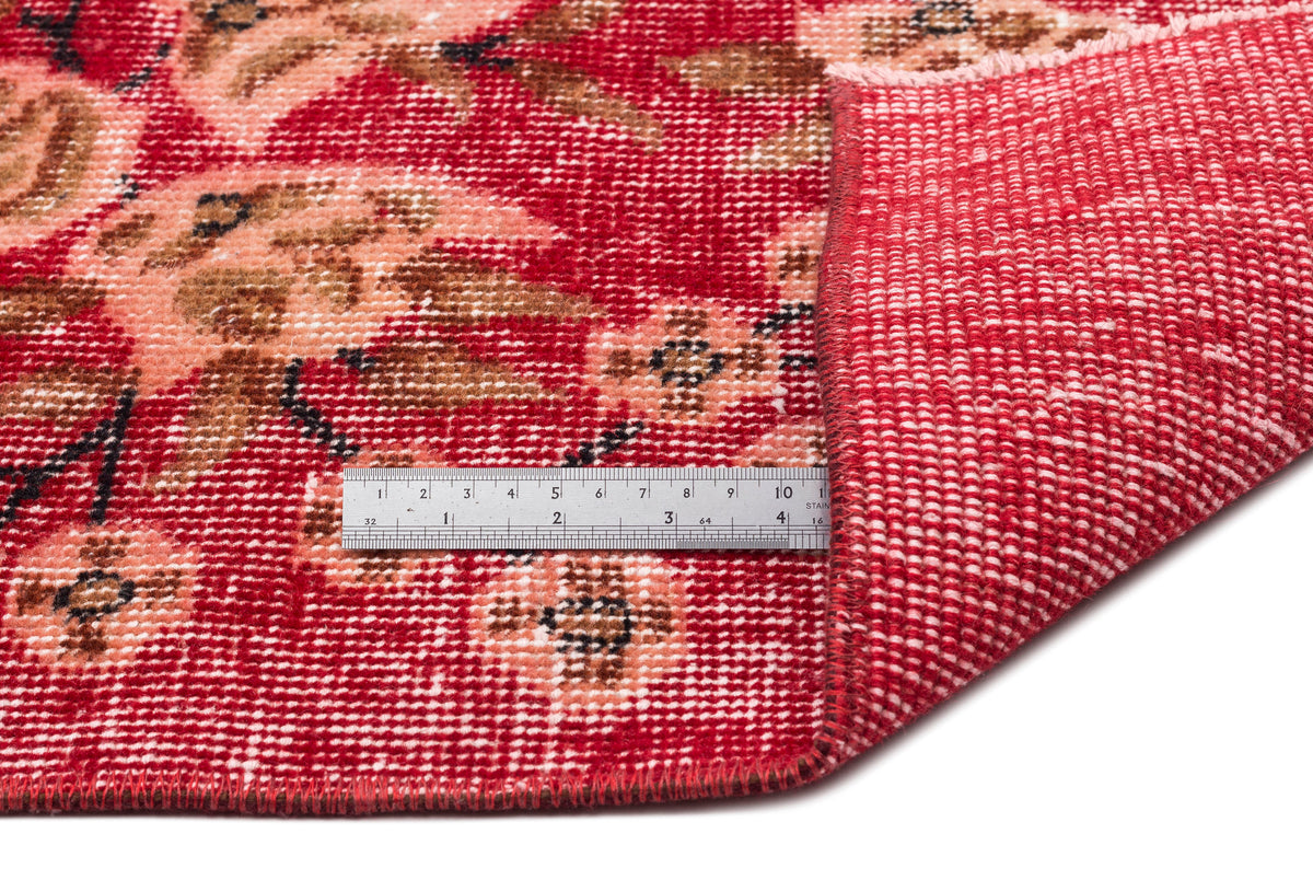 Red and peach floral patterned rug with a folded corner revealing the woven backing and a metal ruler for scale.
