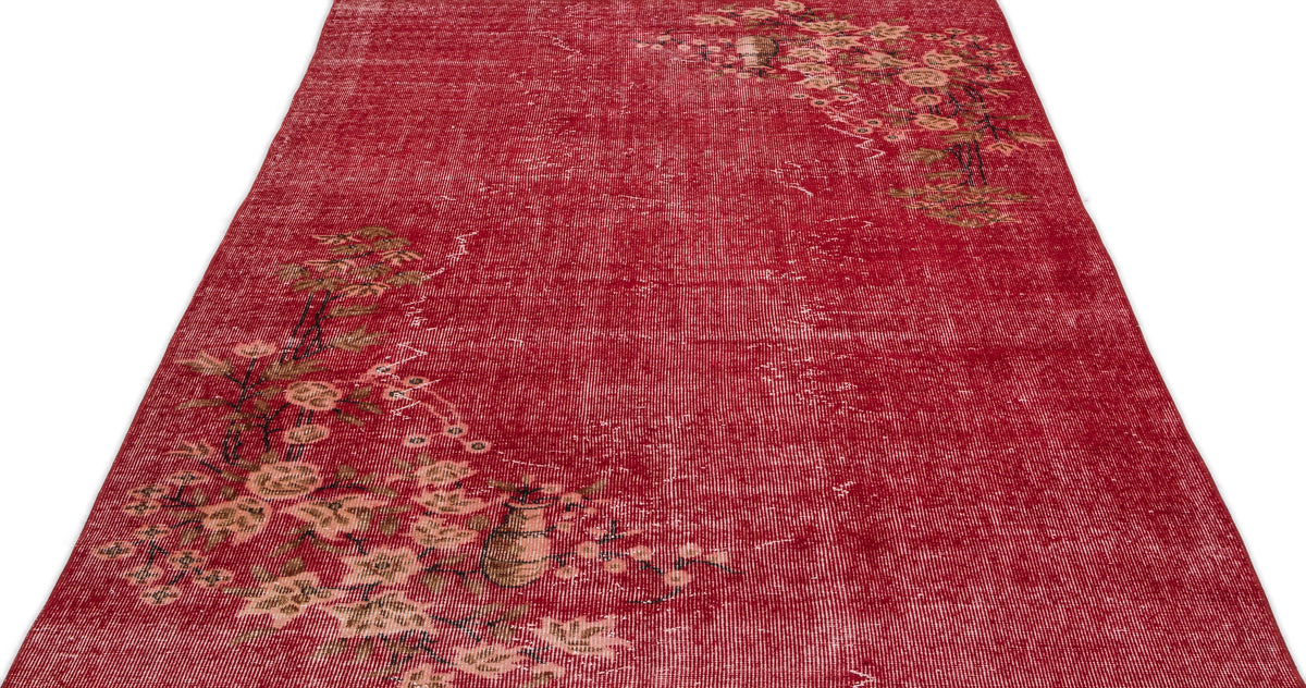 Distressed red rug with a faded floral branch pattern in beige and brown, isolated on a white background.