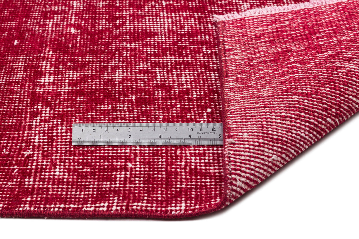 Distressed red and white rug with a folded corner and a metal ruler for scale on a white background.