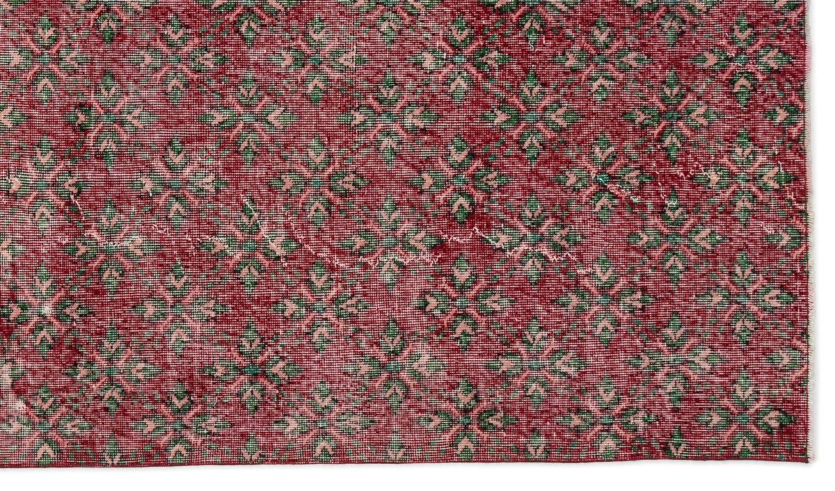 Deep red rug with a repeating geometric floral pattern in muted green and pale pink.