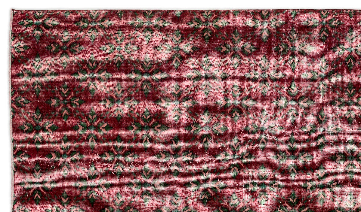 Deep red rug with a repeating green and light pink geometric floral pattern and a distressed texture.