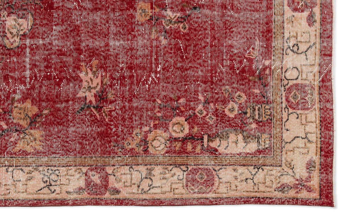 Distressed red rug with a faded floral pattern and a cream-colored border featuring geometric and botanical motifs.