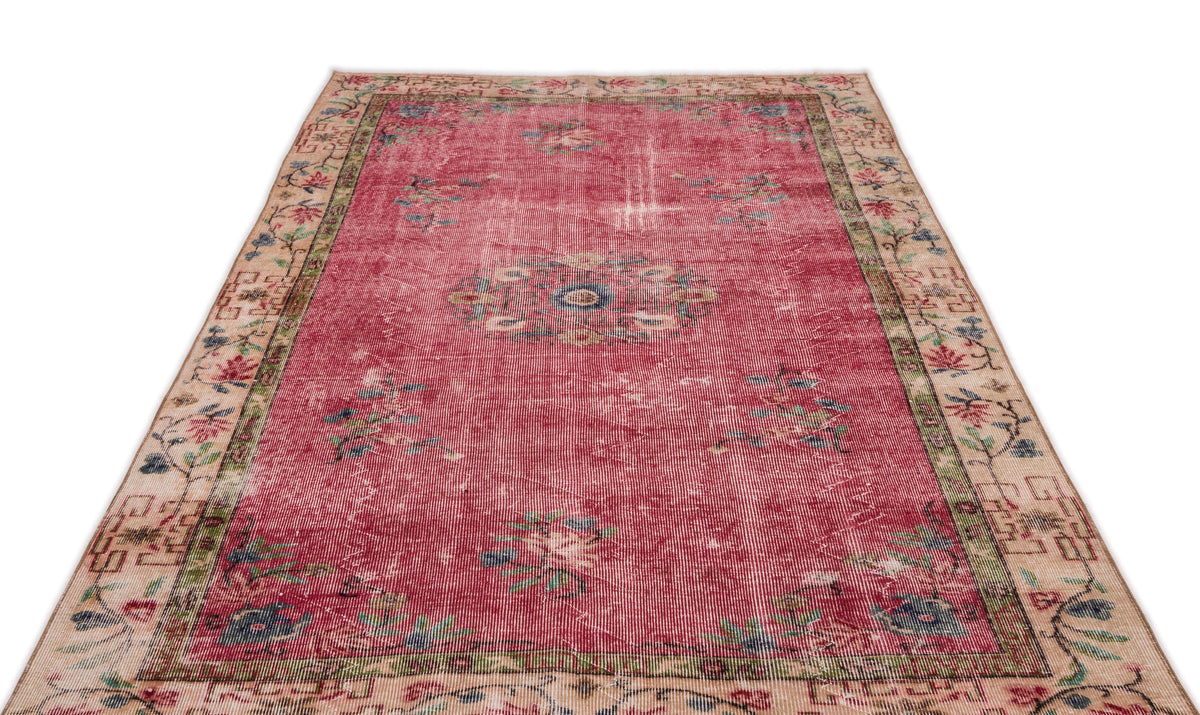 Distressed red vintage rug with a central floral medallion and a beige border featuring botanical motifs.