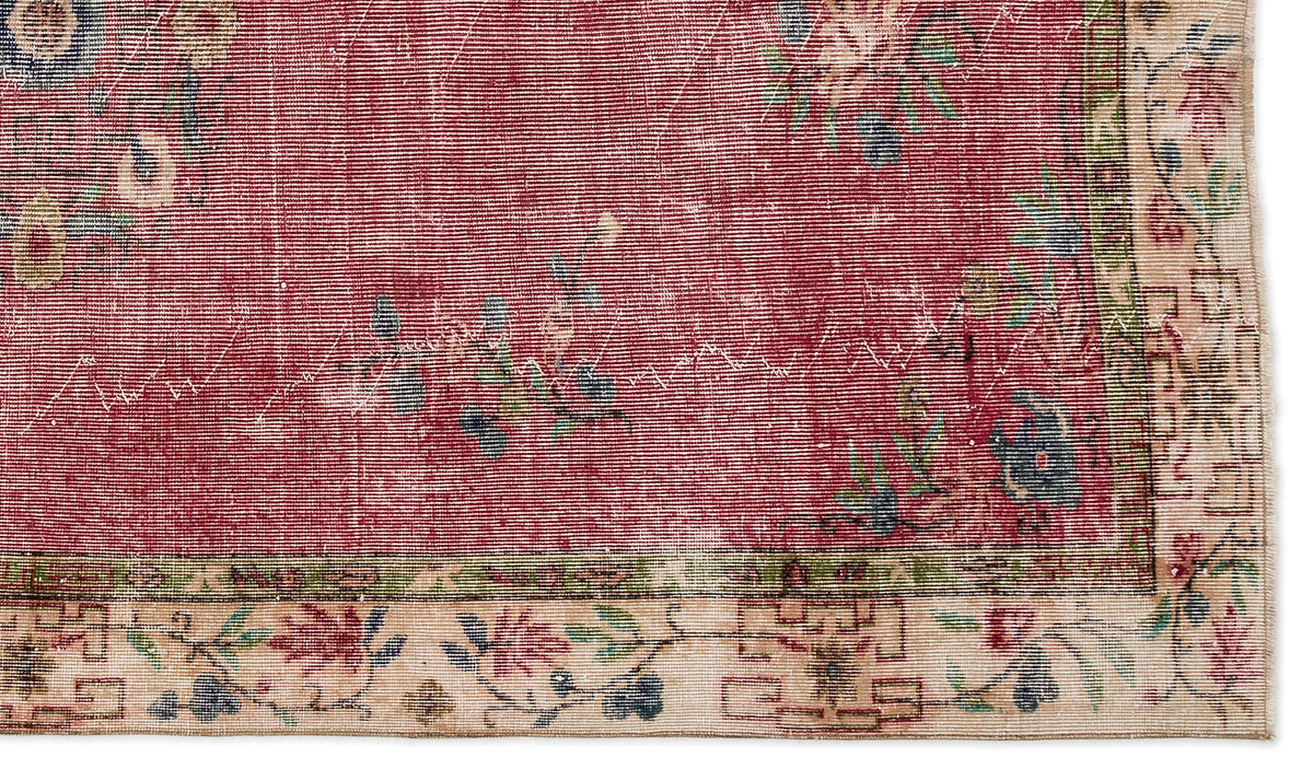 Distressed red rug with a floral pattern and a cream border featuring geometric and botanical motifs.