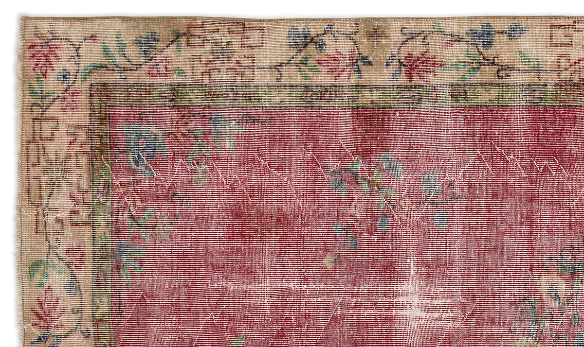 Distressed red rug with a beige floral border and geometric accents, featuring a faded, vintage-style texture.