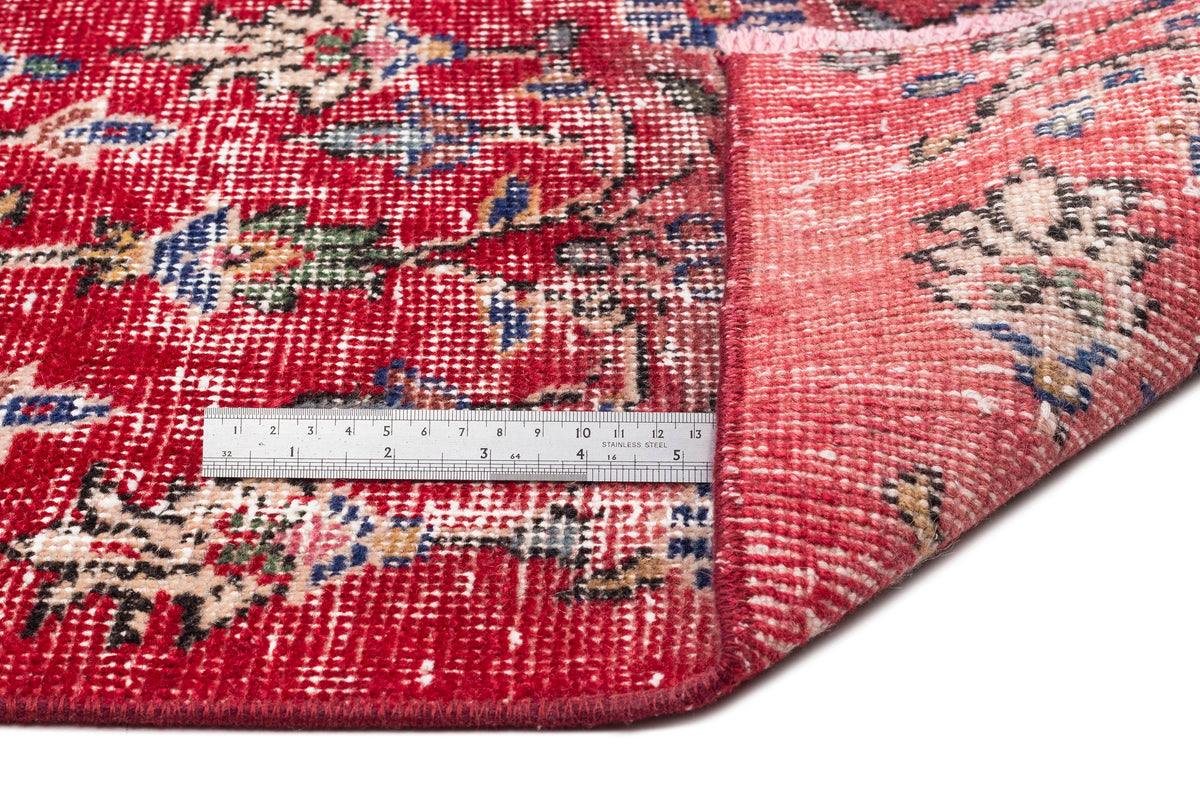 Red vintage-style rug with a distressed floral medallion pattern and a metal ruler showing pile height.