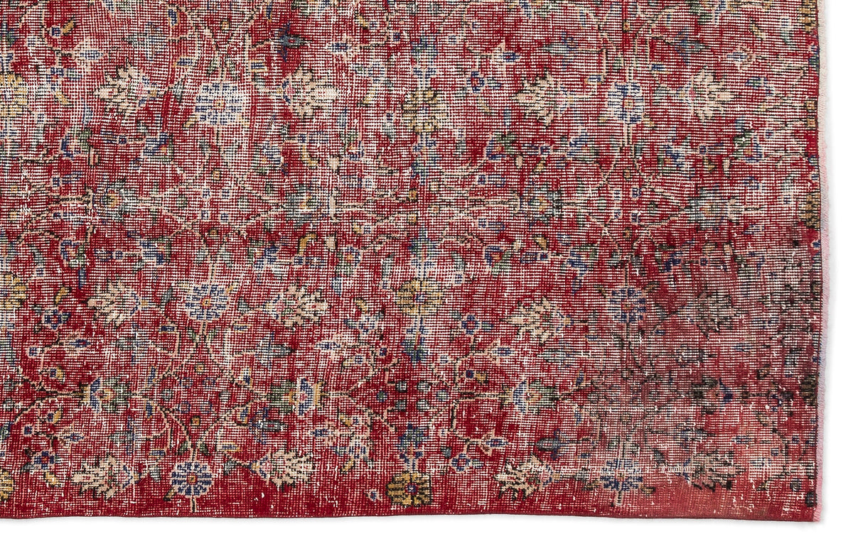 Distressed red rug with a faded floral medallion pattern in blue, cream, and yellow on a white background.