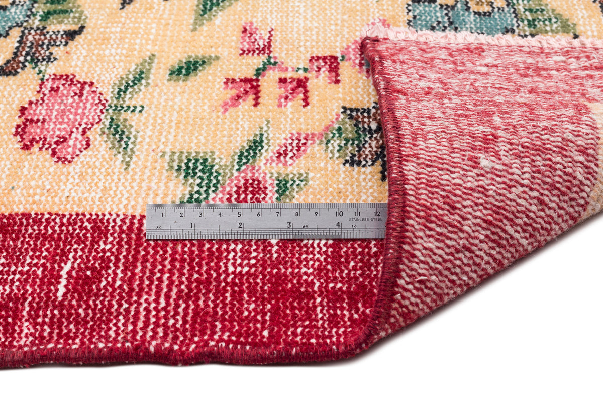 Cream rug with a floral pattern in pink, green, and blue, showing the red underside and a metal ruler for scale.