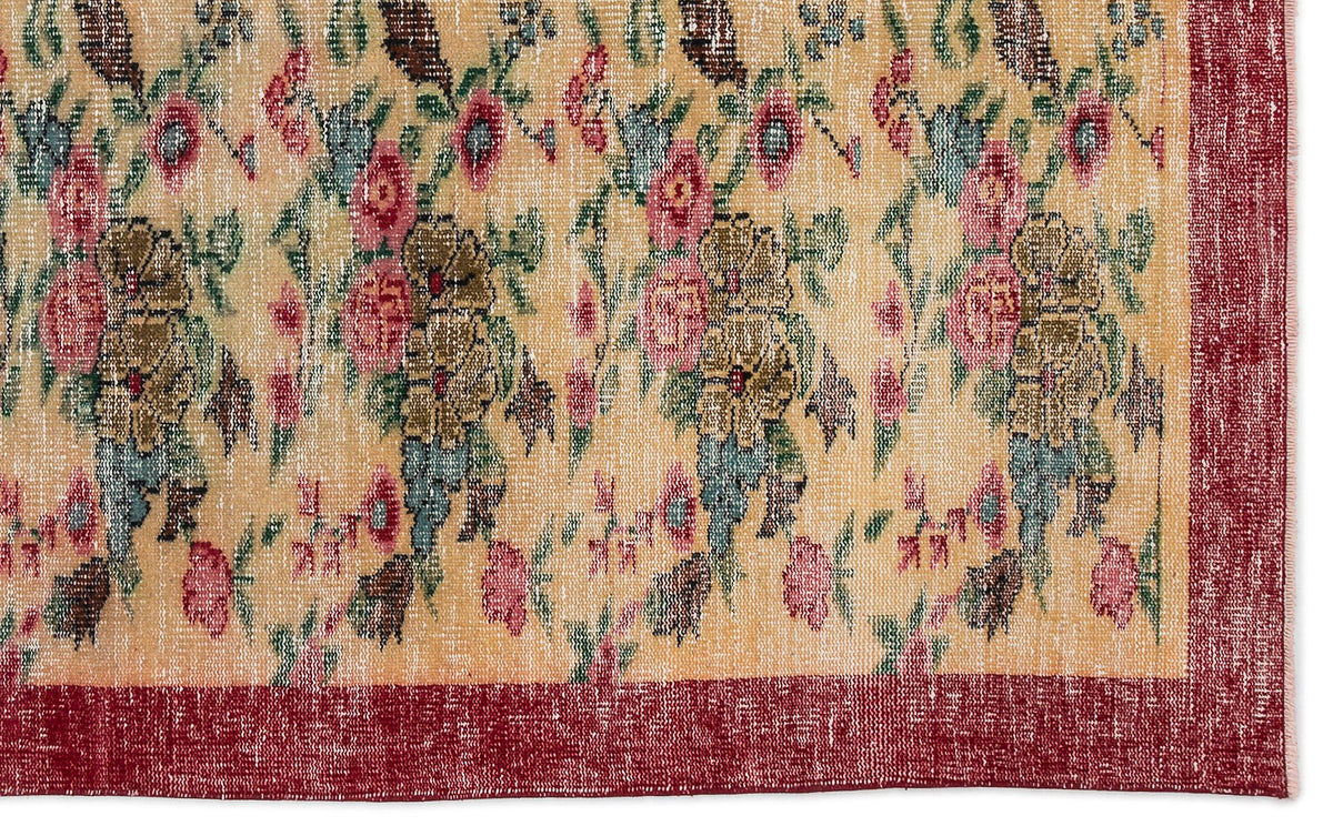 Beige rug with a distressed floral pattern in pink, green, and brown, featuring a solid deep red border.