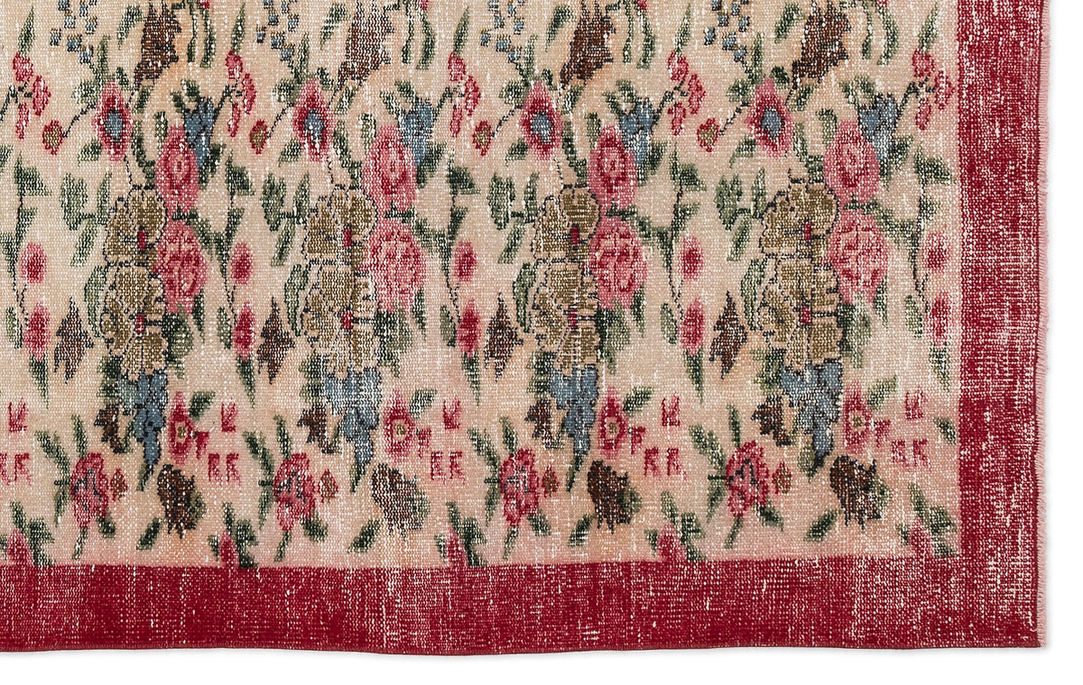 Beige rug with a distressed floral pattern in pink, blue, and olive green, featuring a solid red border.