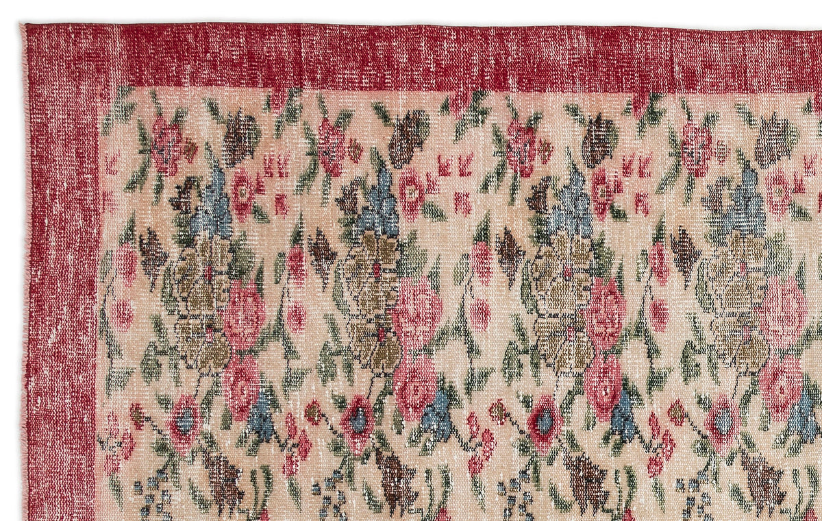 Distressed beige rug with a red border and a repeating floral pattern in shades of pink, blue, and green.