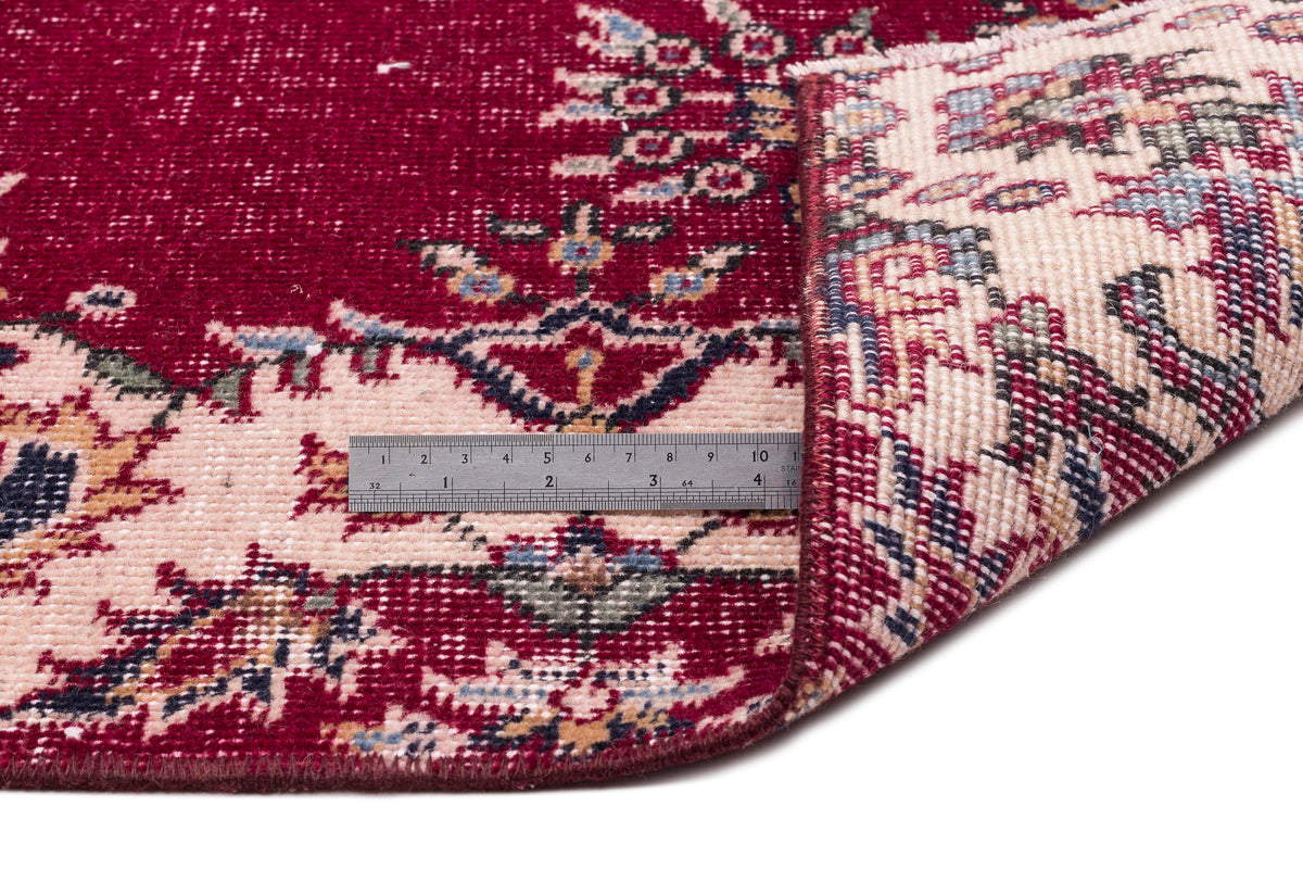 Deep red and cream traditional rug with a floral medallion pattern, shown folded with a metal ruler for scale.