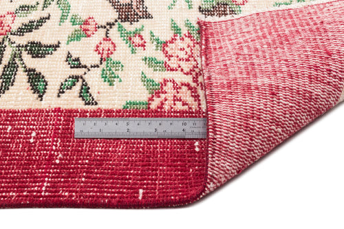 Load image 1 in gallery view. Cream rug with red, green, and brown floral pattern, folded to show the red woven backing and a metal ruler for scale.