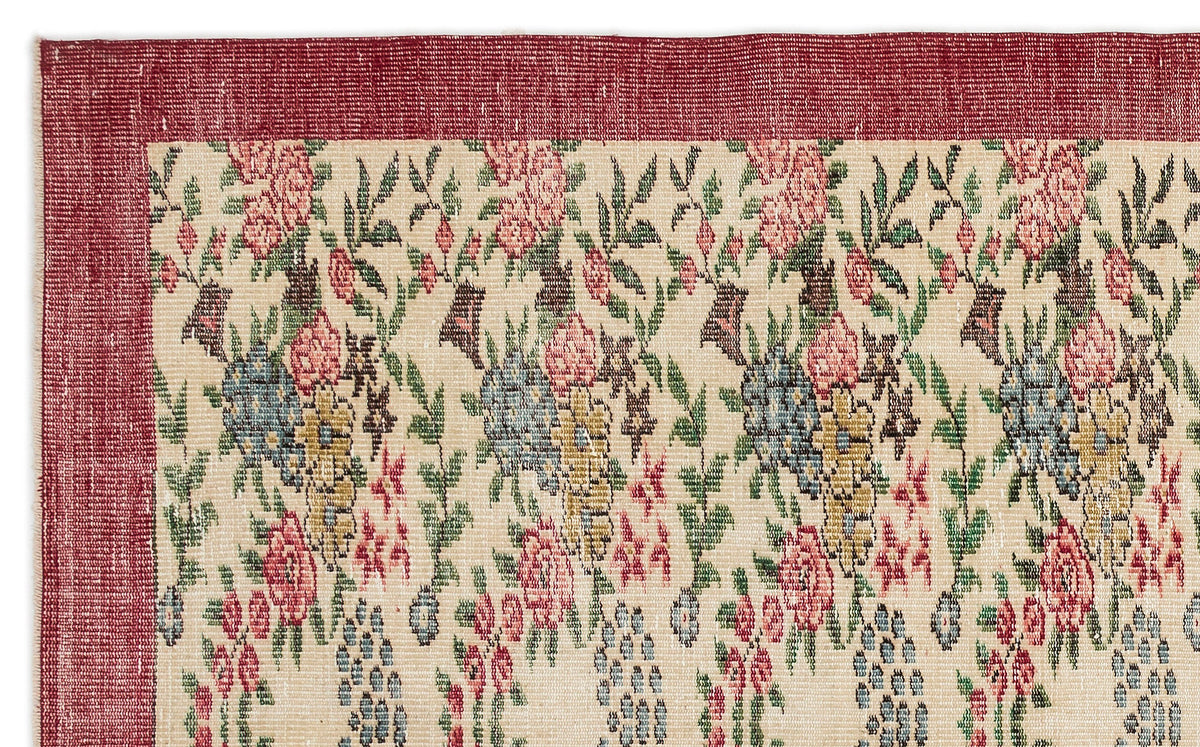 Cream rug with a red border and a repeating floral pattern in shades of pink, blue, yellow, and green.