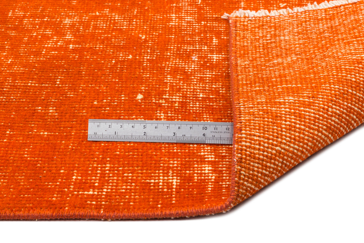 Bright orange distressed rug with a white woven backing, shown with a metal ruler for scale.