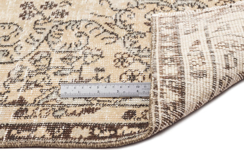 Load image 1 in gallery view. A close-up of the Preutata - Vintage Medallion Rug (5'4 x 8'11) shows its beige and brown pattern, one corner folded, and a metal ruler on top indicating a length of about 15 centimeters for scale.