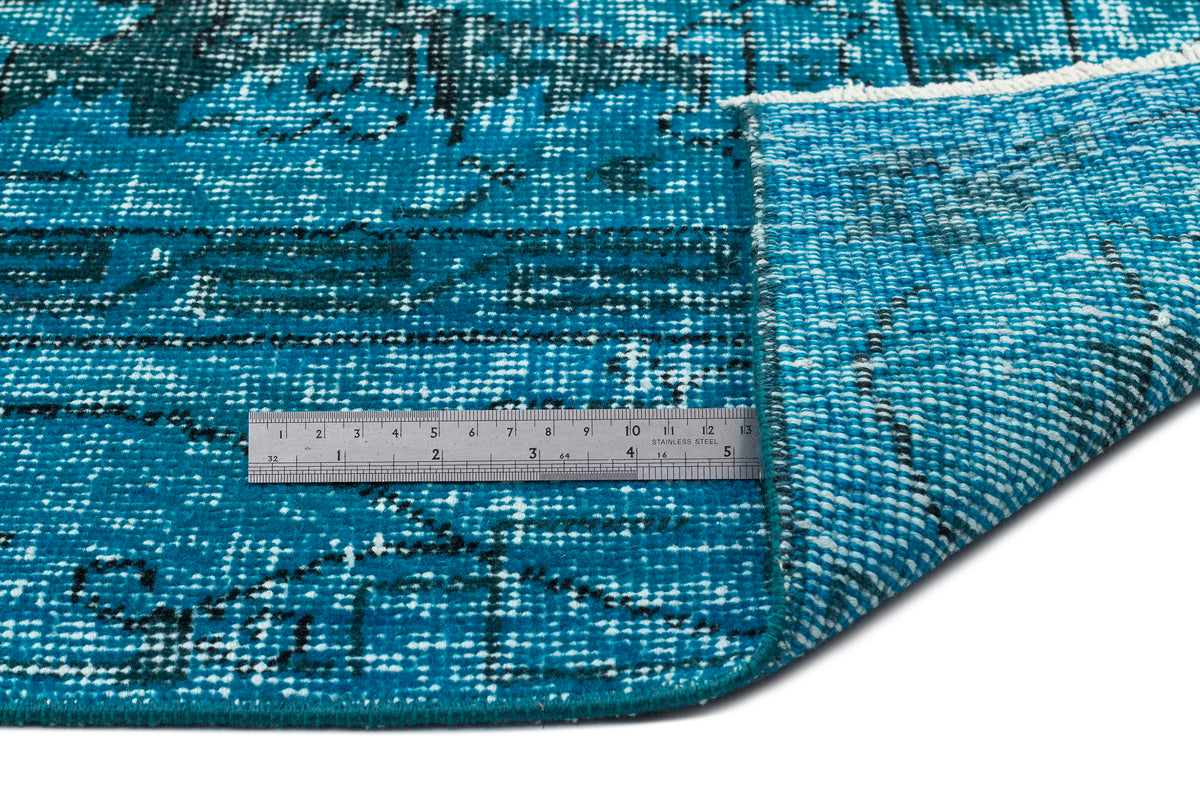 Teal and black distressed patterned rug with a folded corner, shown with a metal ruler for scale on a white background.