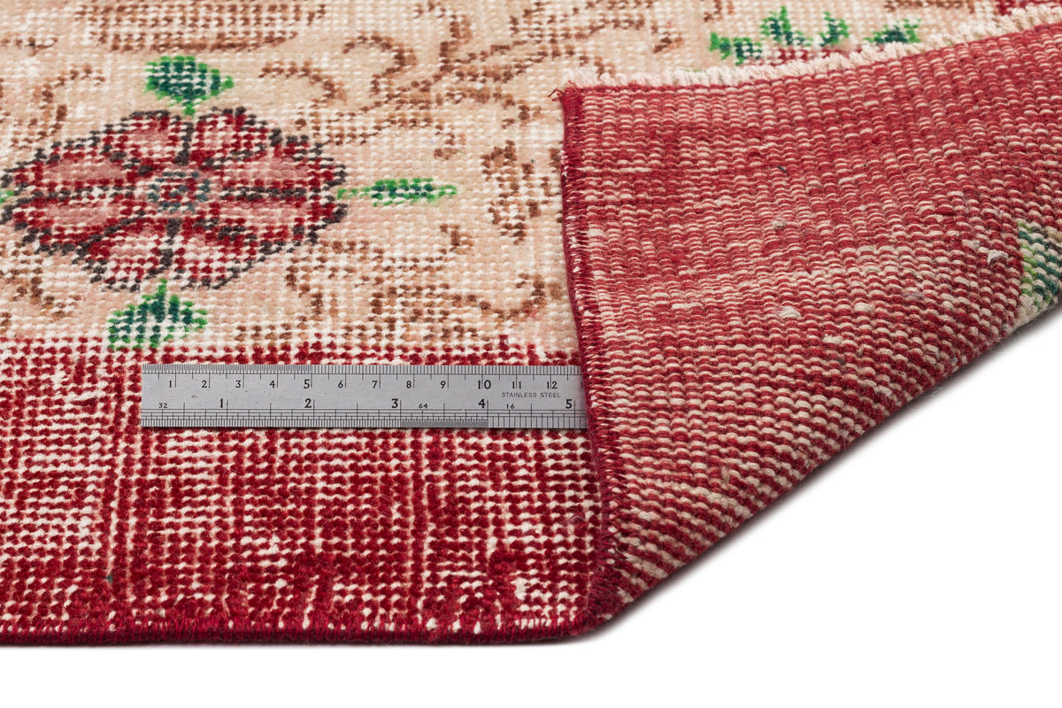 Beige and red vintage-style rug with a floral medallion pattern, shown folded with a metal ruler for scale.