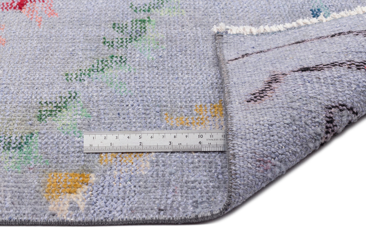 Light blue rug with small, scattered multi-colored abstract motifs and a metal ruler for scale on a white background.