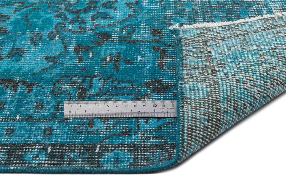Teal and charcoal distressed medallion rug with a folded corner showing the backing and a metal ruler for scale.