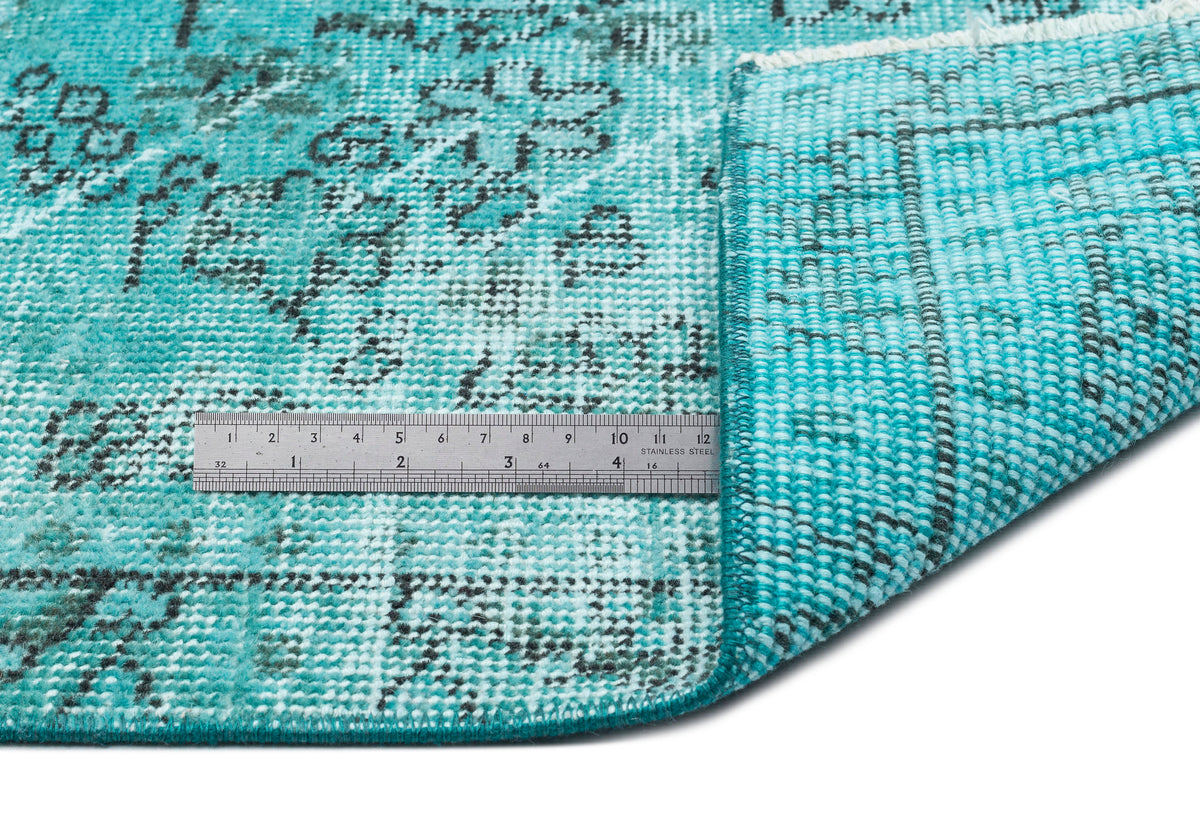 Turquoise and black distressed floral rug with a folded corner and a metal ruler for scale on a white background.