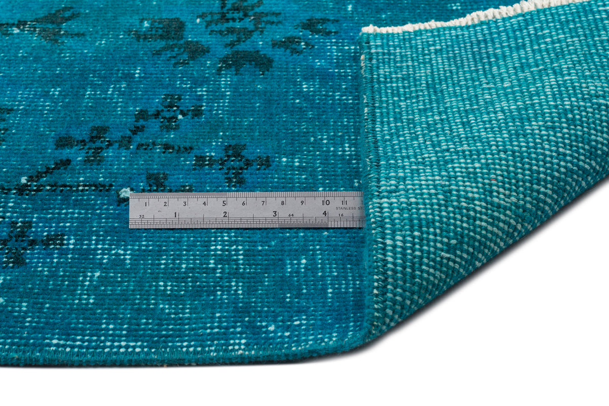 Teal rug with a distressed floral pattern, showing the woven backing and a metal ruler for scale.